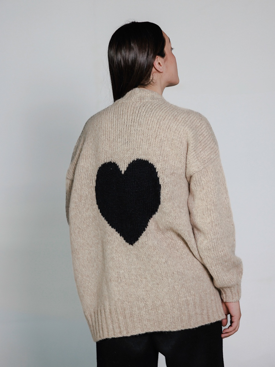 Person wearing a beige sweater with a black heart design on the back against a plain background