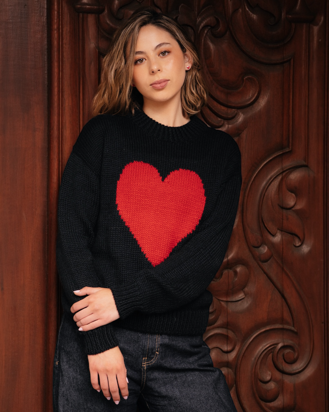 Woman wearing a black sweater with a red heart design against a decorative brown background
