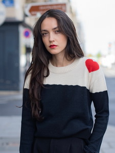 Dora sweater, baby alpaca, color-block black and white with red heart on the shoulder on model in city street 