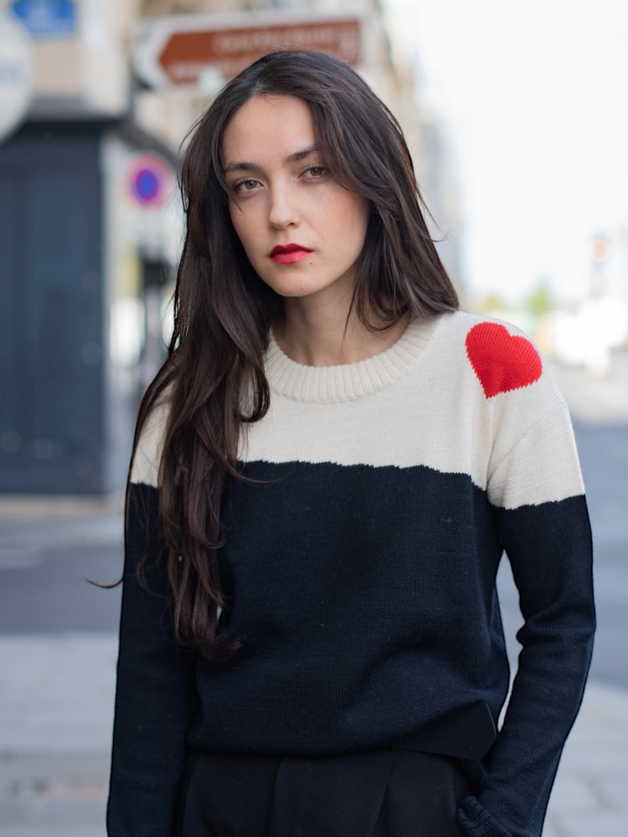 Dora sweater, baby alpaca, color-block black and white with red heart on the shoulder on model in city street 