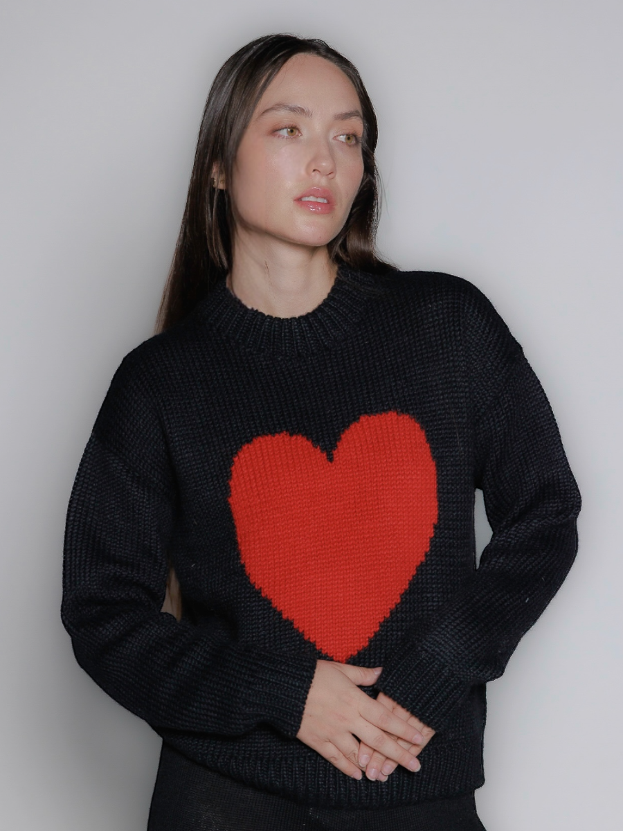model wearing a black sweater with a red heart design against a plain background