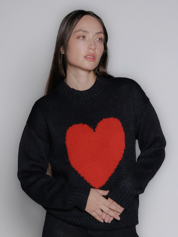 model wearing a black sweater with a red heart design against a plain background