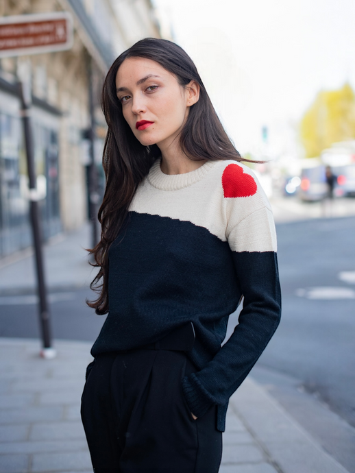 Dora sweater, baby alpaca, color-block black and white with red heart on the shoulder on model in city street