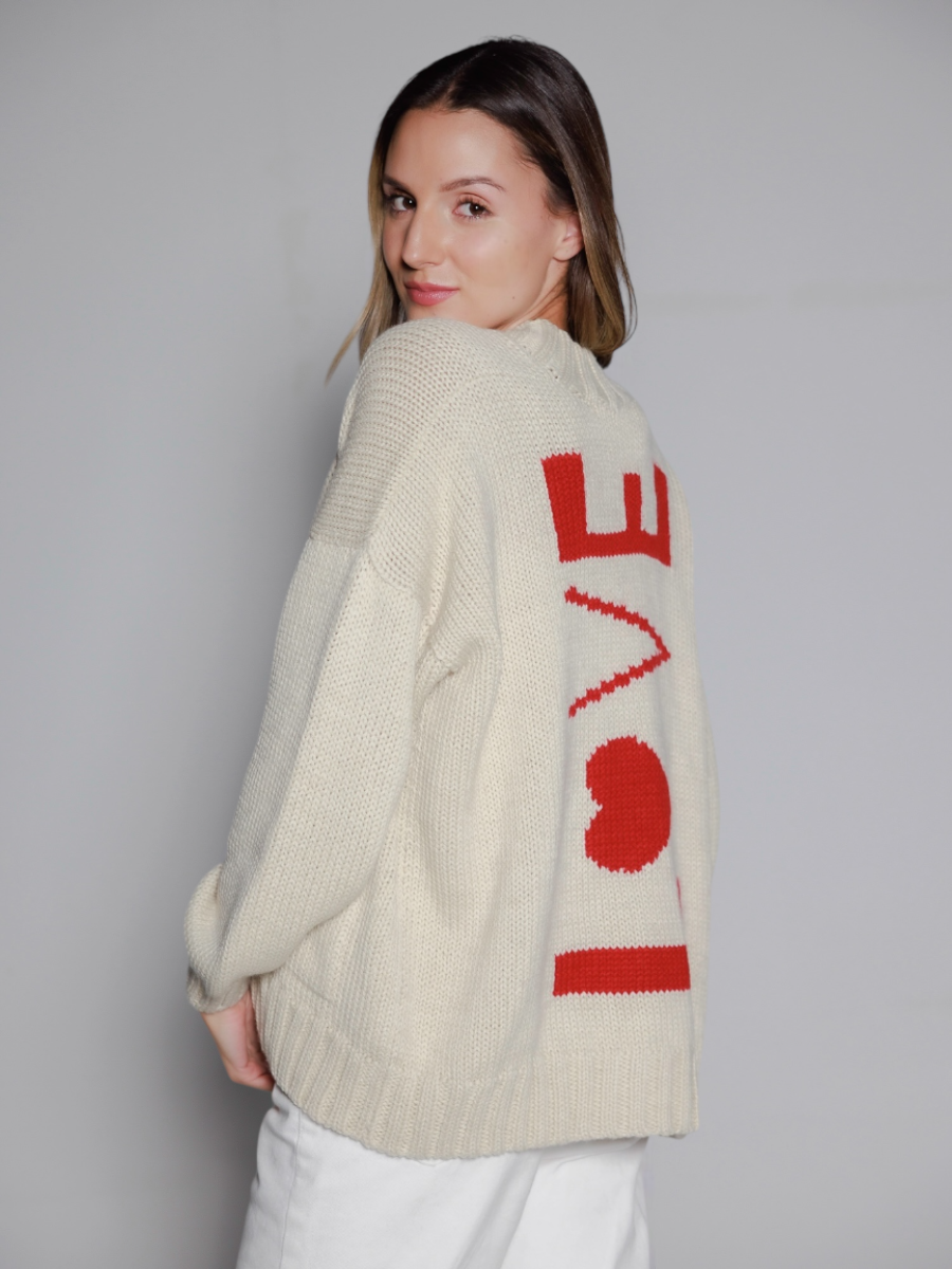 White alpaca sweater featuring a bold red “LOVE” motif with a heart design on the back, shown here on a model in a white background.