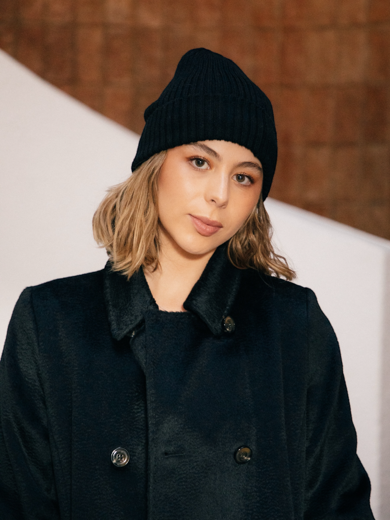 Person wearing a black alpaca coat and beanie against a neutral background