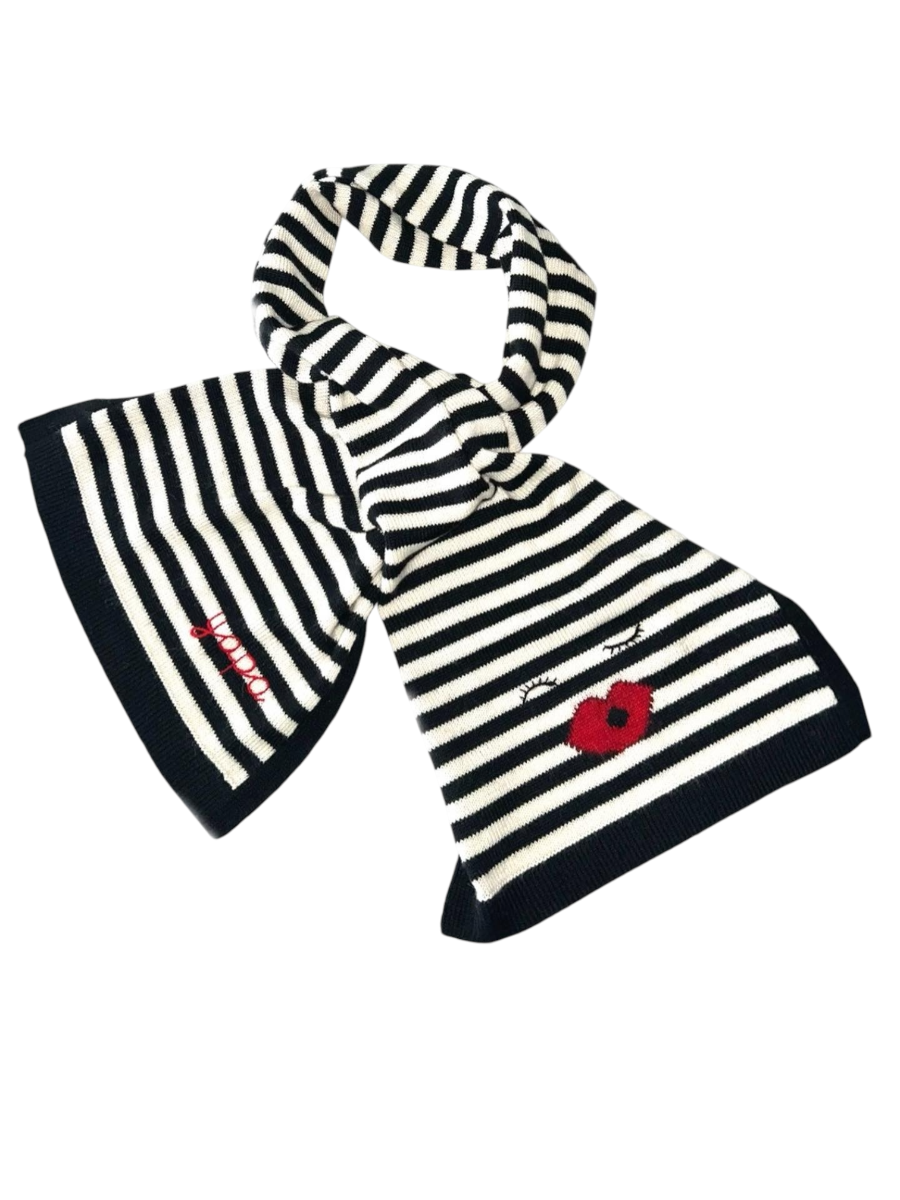 Black-and-white striped alpaca scarf featuring an embroidered face motif with closed eyes and red lips styled with a yapa sweater, shown on a model against an outdoor background.