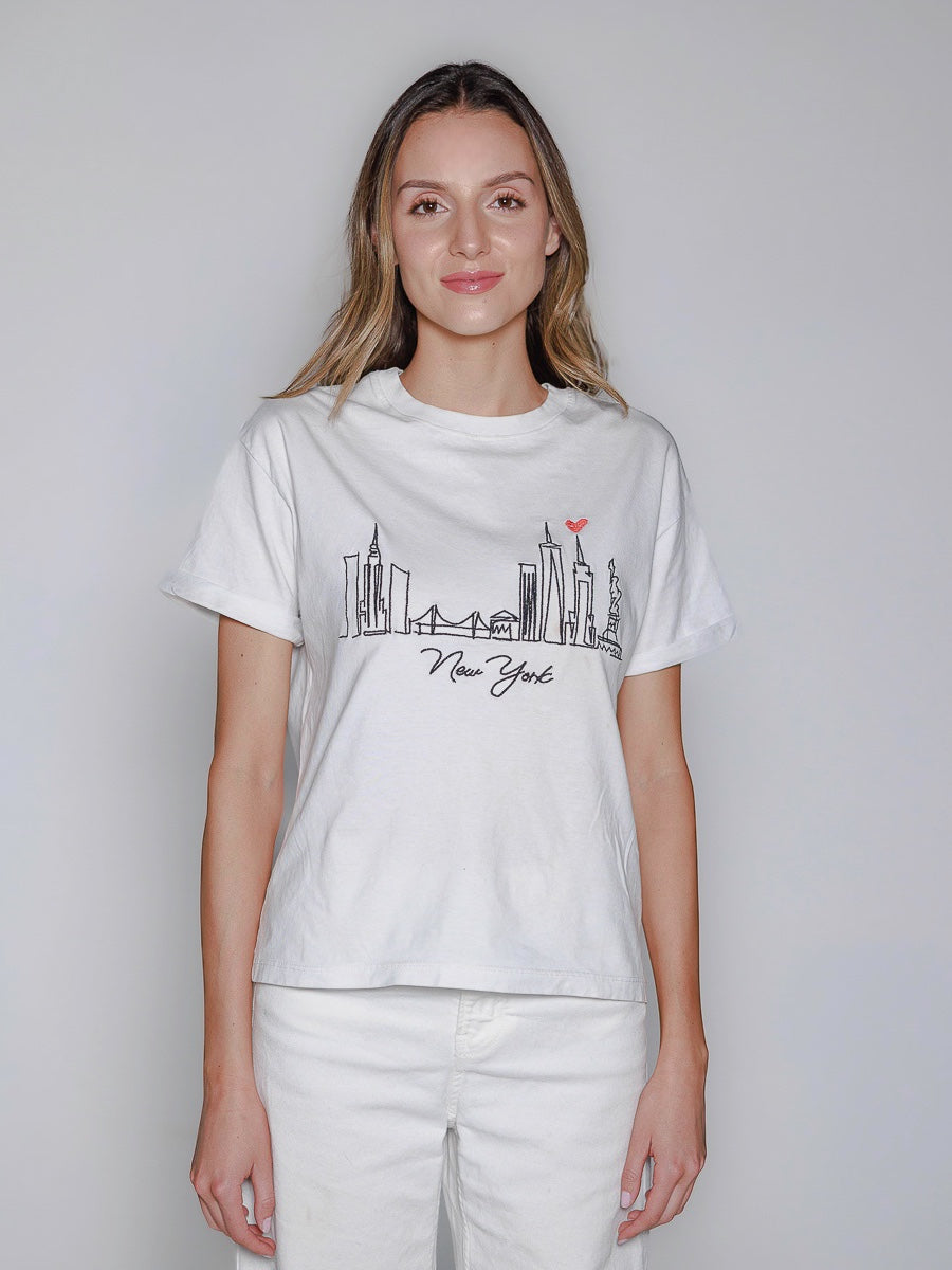 Woman wearing a white t-shirt with a New York skyline design on a plain background