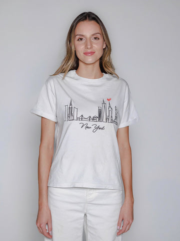 Woman wearing a white t-shirt with a New York skyline design on a plain background