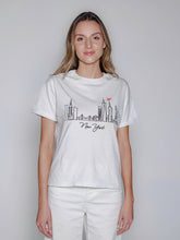 Cargar imagen en el visor de la galería, Woman wearing a white t-shirt with a New York skyline design on a plain background

