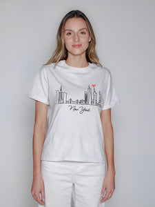 Woman wearing a white t-shirt with a New York skyline design on a plain background
