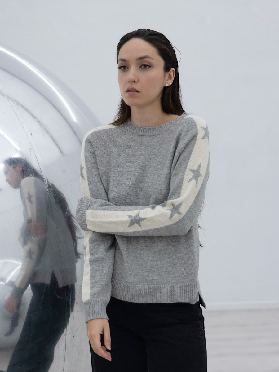 grey alpaca sweater with stars on the sleeves on model with an art gallery background