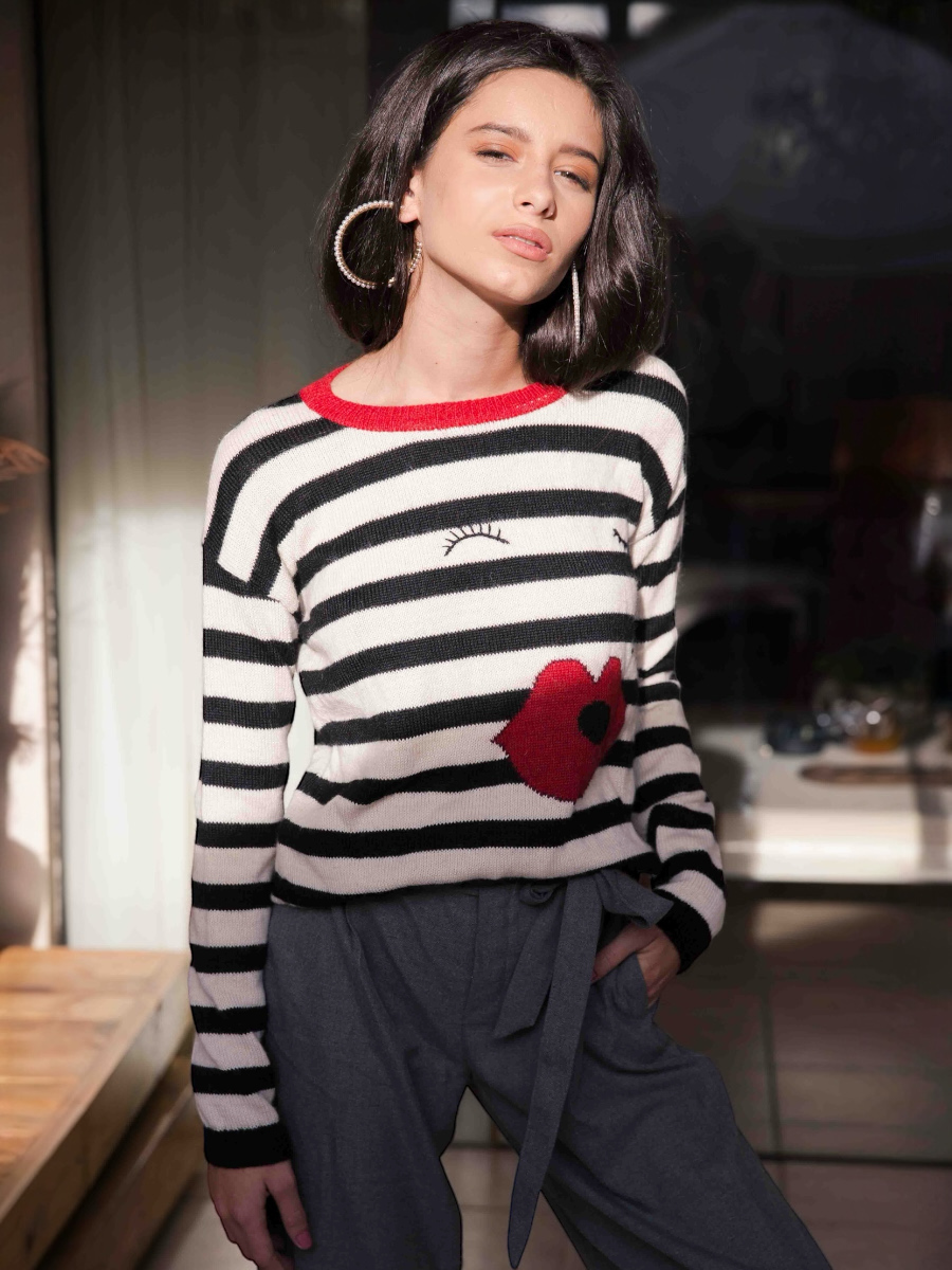Woman wearing a black and white striped sweater with a red heart design indoors.