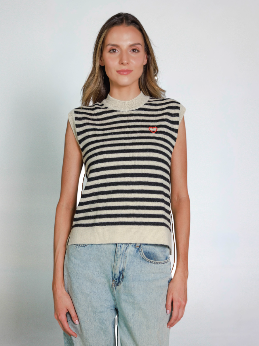Woman wearing a striped sleeveless knitted vest and jeans on a plain background