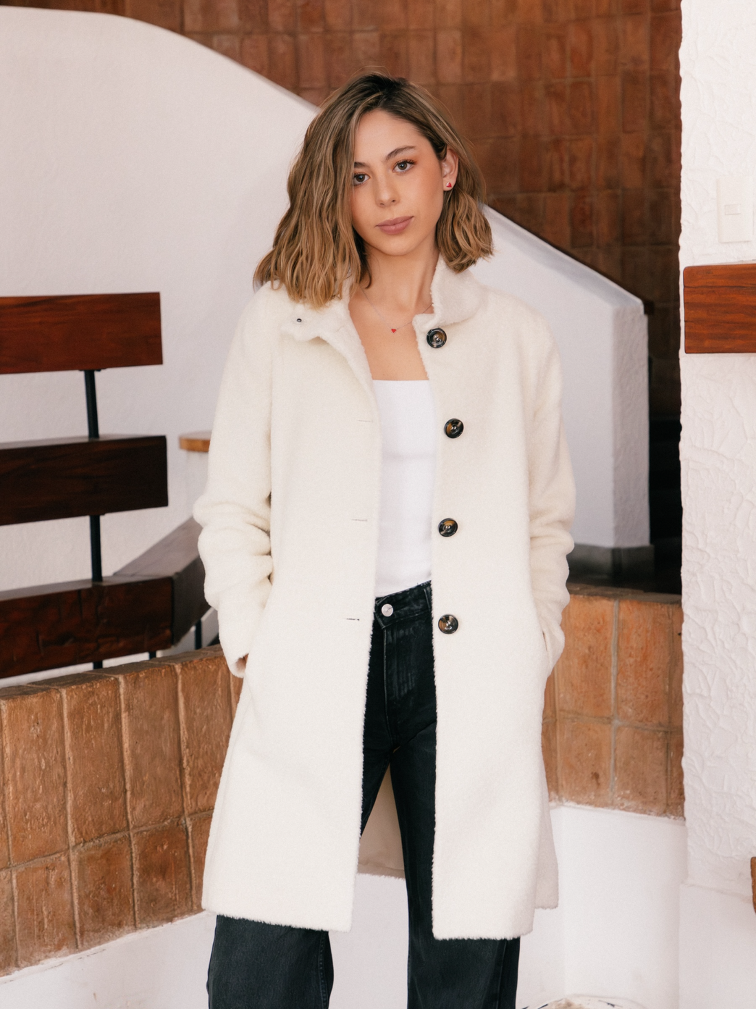 Woman wearing a white alpaca coat with black buttons in an indoor setting.