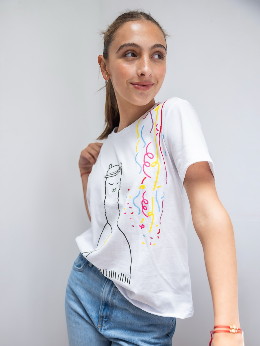 White cotton t-shirt featuring an embroidered alpaca in traditional attire with colorful confetti details on the side, worn by a model