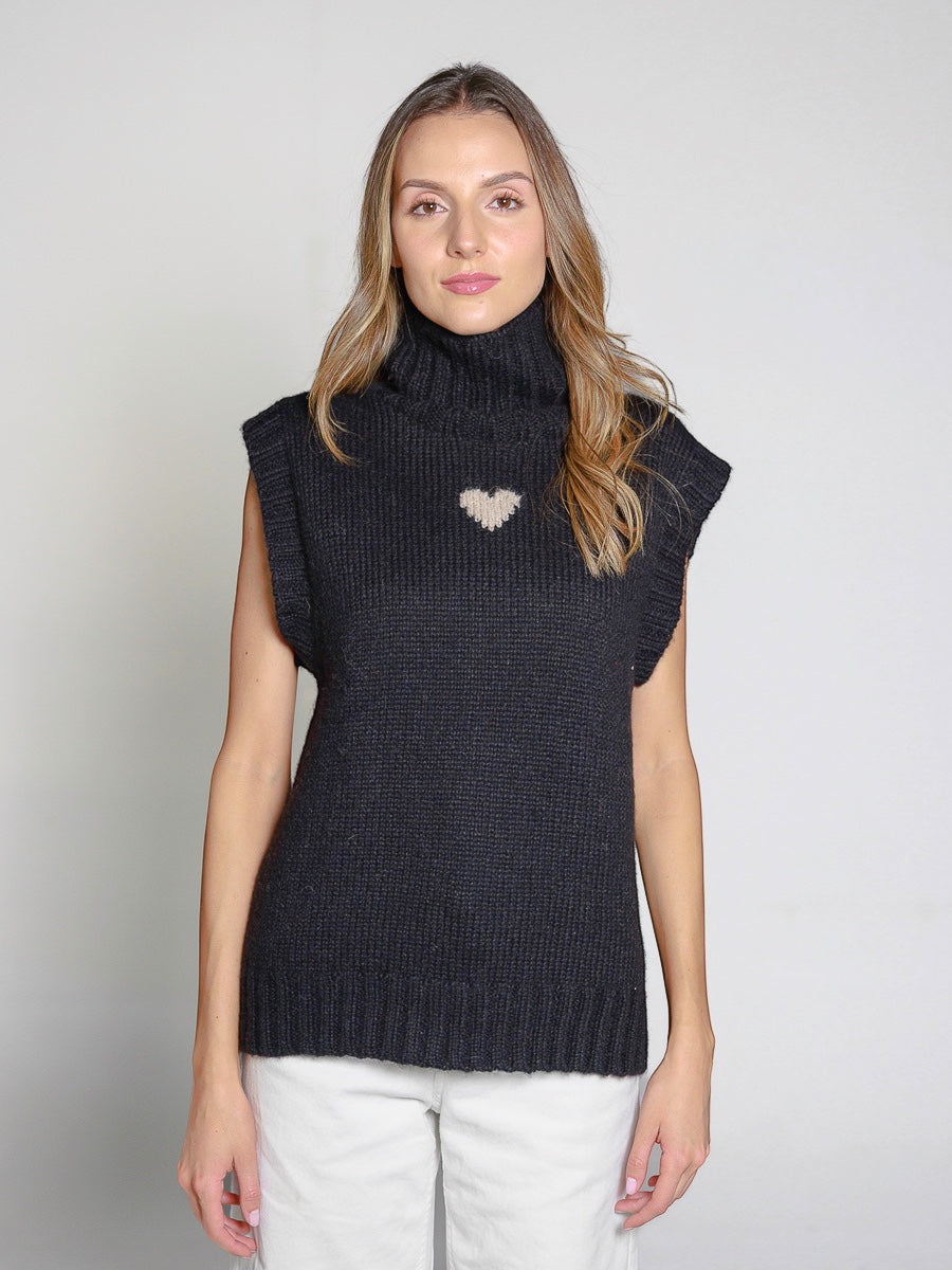 Woman wearing a black knitted sweater vest with a heart design on a plain background