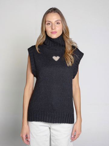 Woman wearing a black knitted sweater vest with a heart design on a plain background