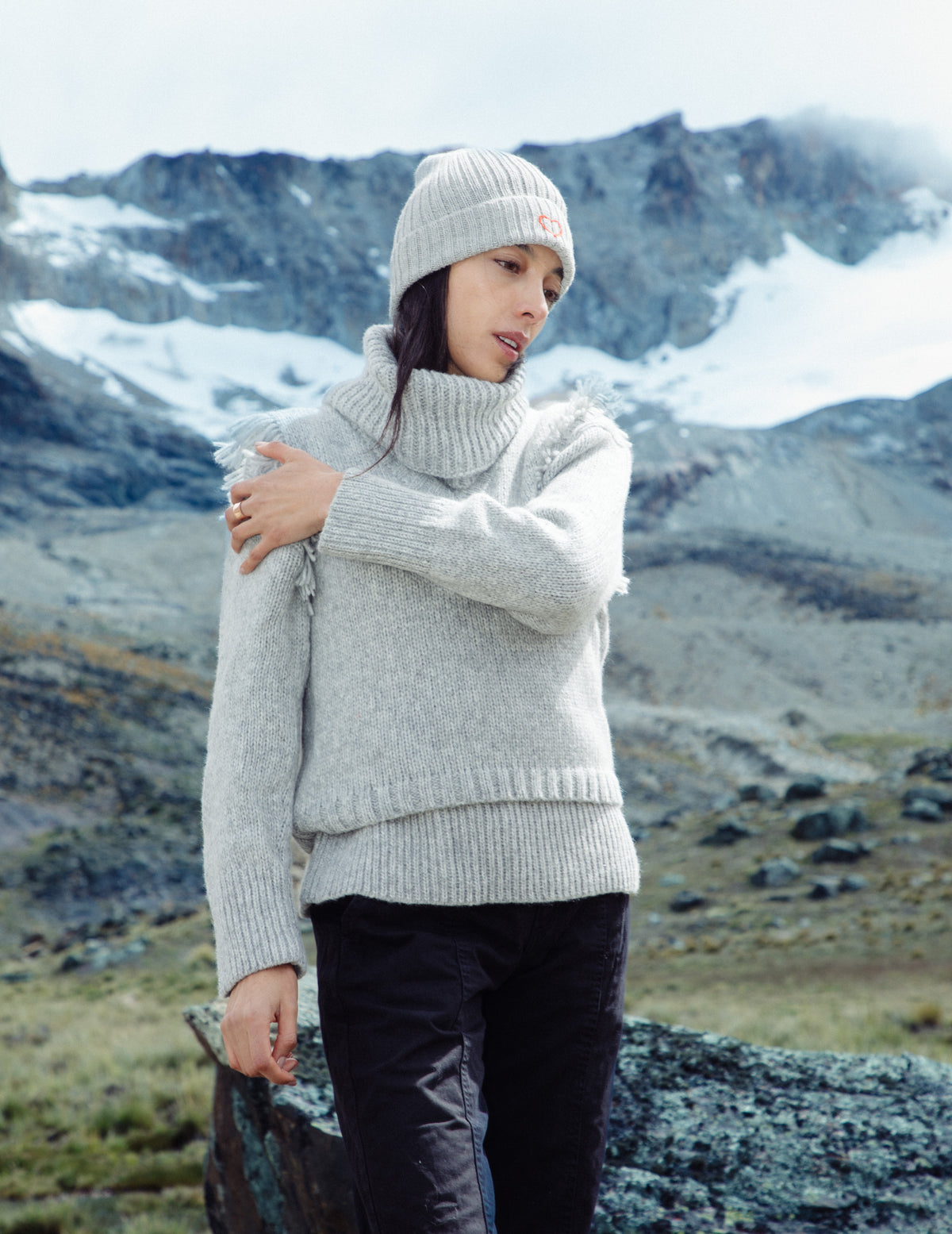 Person wearing a light gray sweater and white knit hat in a mountainous landscape