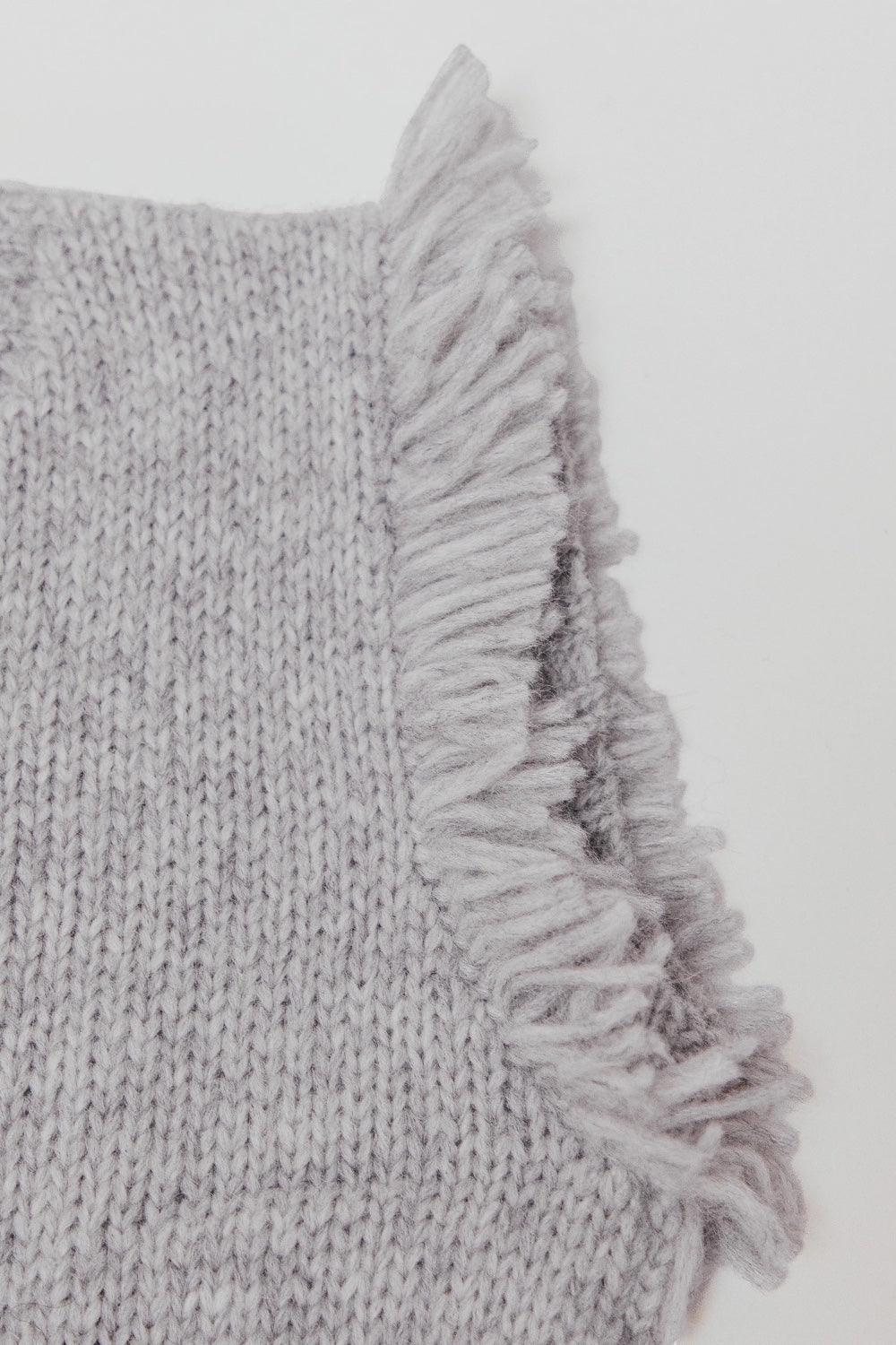Close-up of a light gray knit sweater vest with fringes