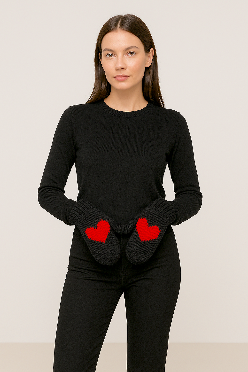 Woman wearing black mittens with a red heart a  black long-sleeve top and pants  on a plain background