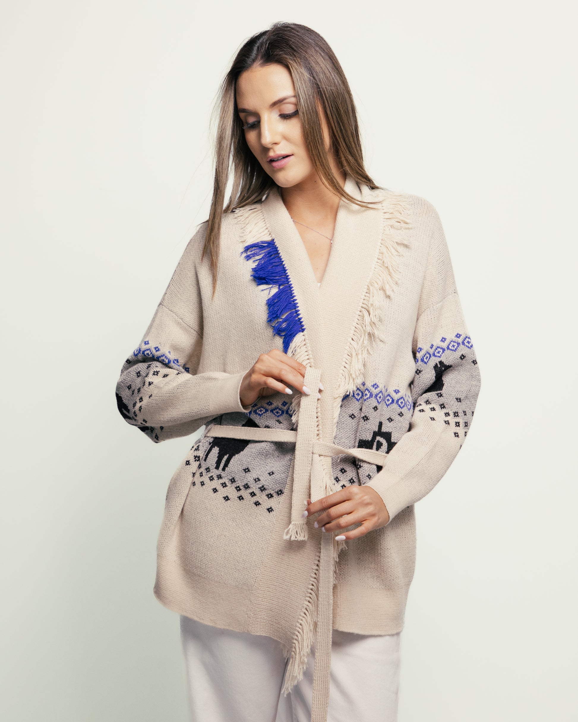 Woman wearing a stylish beige cardigan with blue and black patterns on a plain background