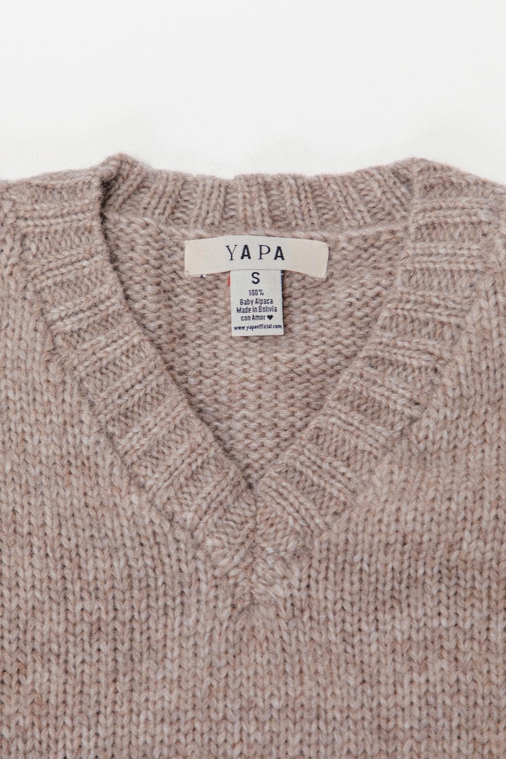 Close-up of a light gray knit sweater with a ribbed V-neck collar and a visible YAPA brand label.