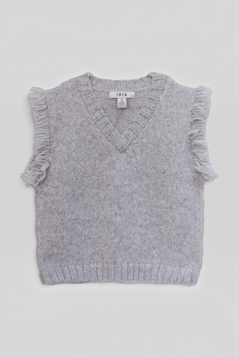 A light gray knit sweater vest with fringed sleeve edges and a V-neck, laid flat against a light gray background. The brand label reads Yapa