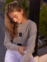 Load image into Gallery viewer, grey sweater decorated with a turkish eye, heart and a star on a model in city street
