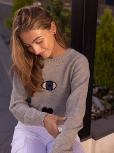 grey sweater decorated with a turkish eye, heart and a star on a model in city street
