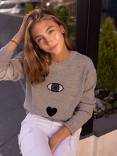 Load image into Gallery viewer, grey sweater decorated with a turkish eye, heart and a star on a model in city street
