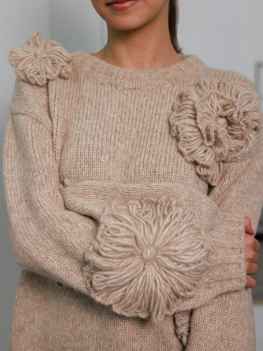 Woman wearing a beige sweater with floral embellishments