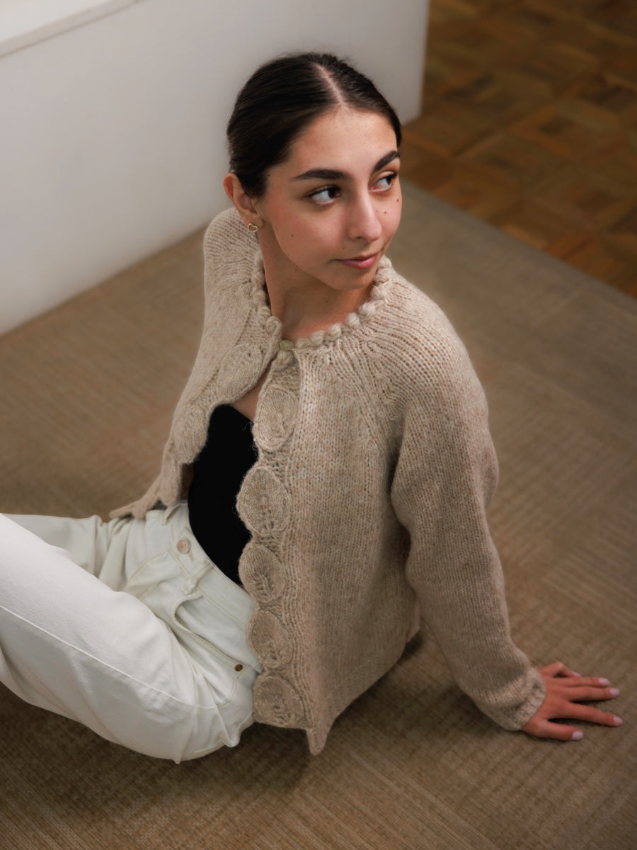 Woman sitting on a wooden floor wearing a beige knitted cardigan. Must have cardigans.
