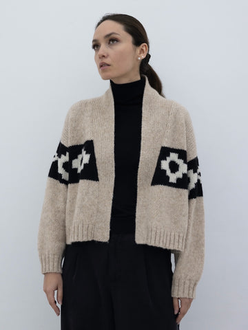 beige llama cardigan with black and white cross pattern, worn by a model on a plain background