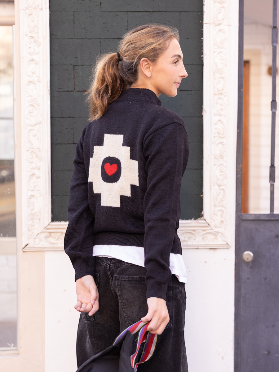 black alpaca jacket  featuring a white cross pattern with a red heart design on the back, worn by a model on the street