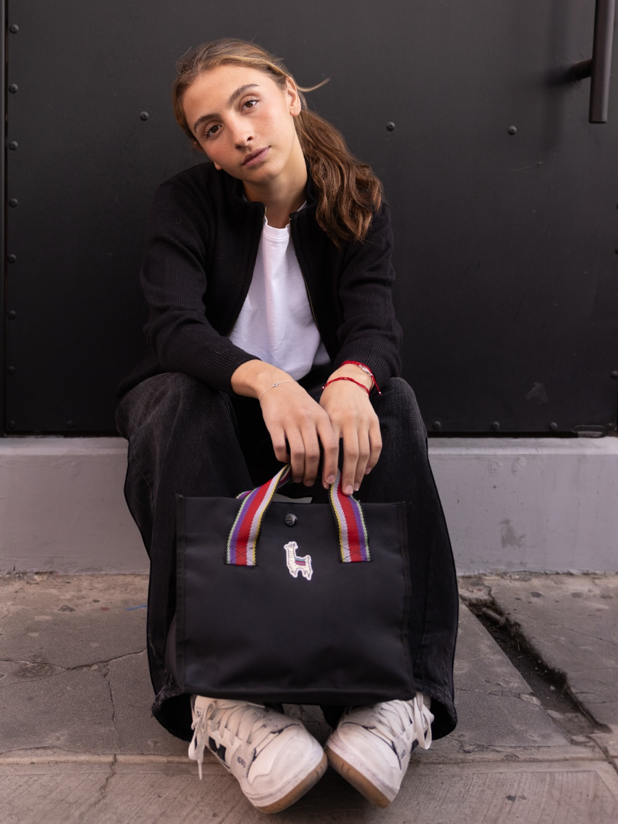 black alpaca jacket featuring a white cross pattern with a red heart design on the back, worn by a model on the street