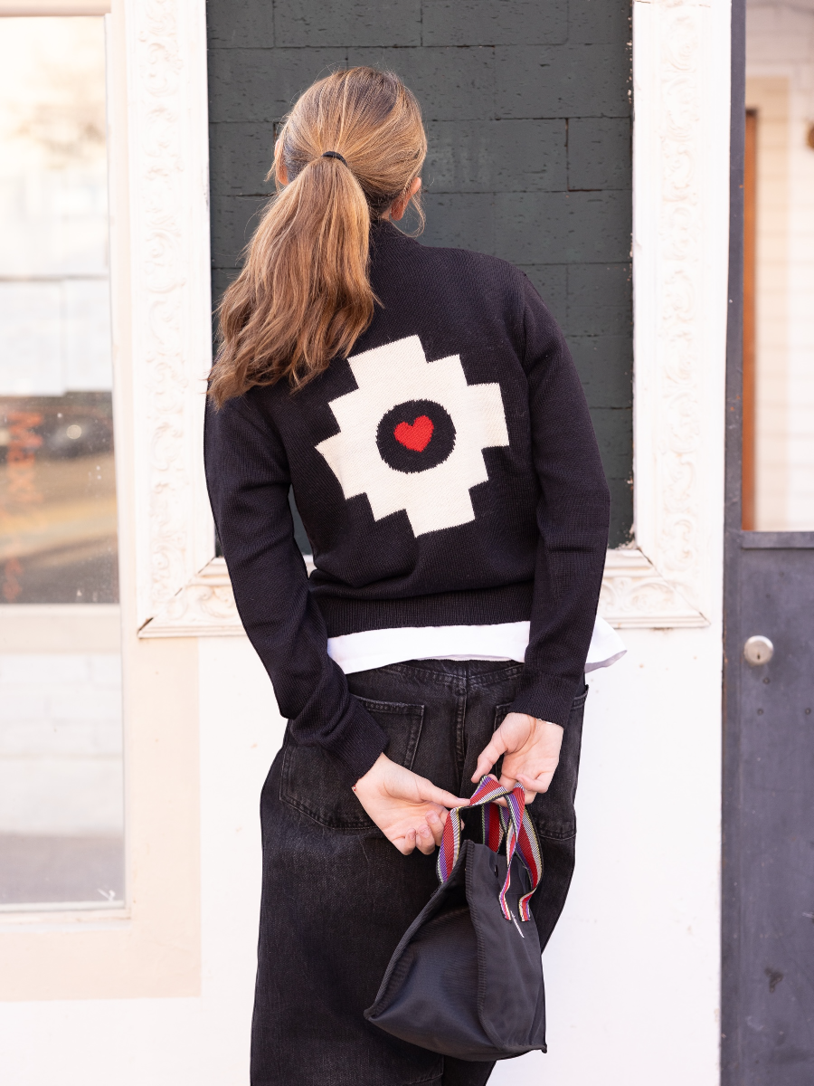 black alpaca jacket  featuring a white cross pattern with a red heart design on the back, worn by a model on the street