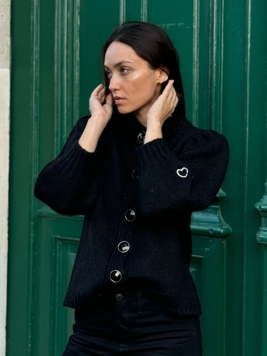 black chunky alpaca knitted cardigan with large round buttons, worn by a model against a green door