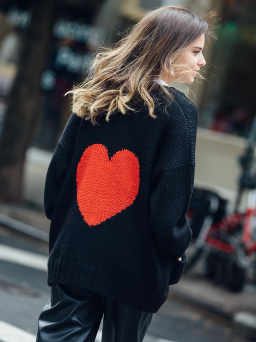 Woman wearing a black knitted cardigan with a red heart in the back walking around New York City
