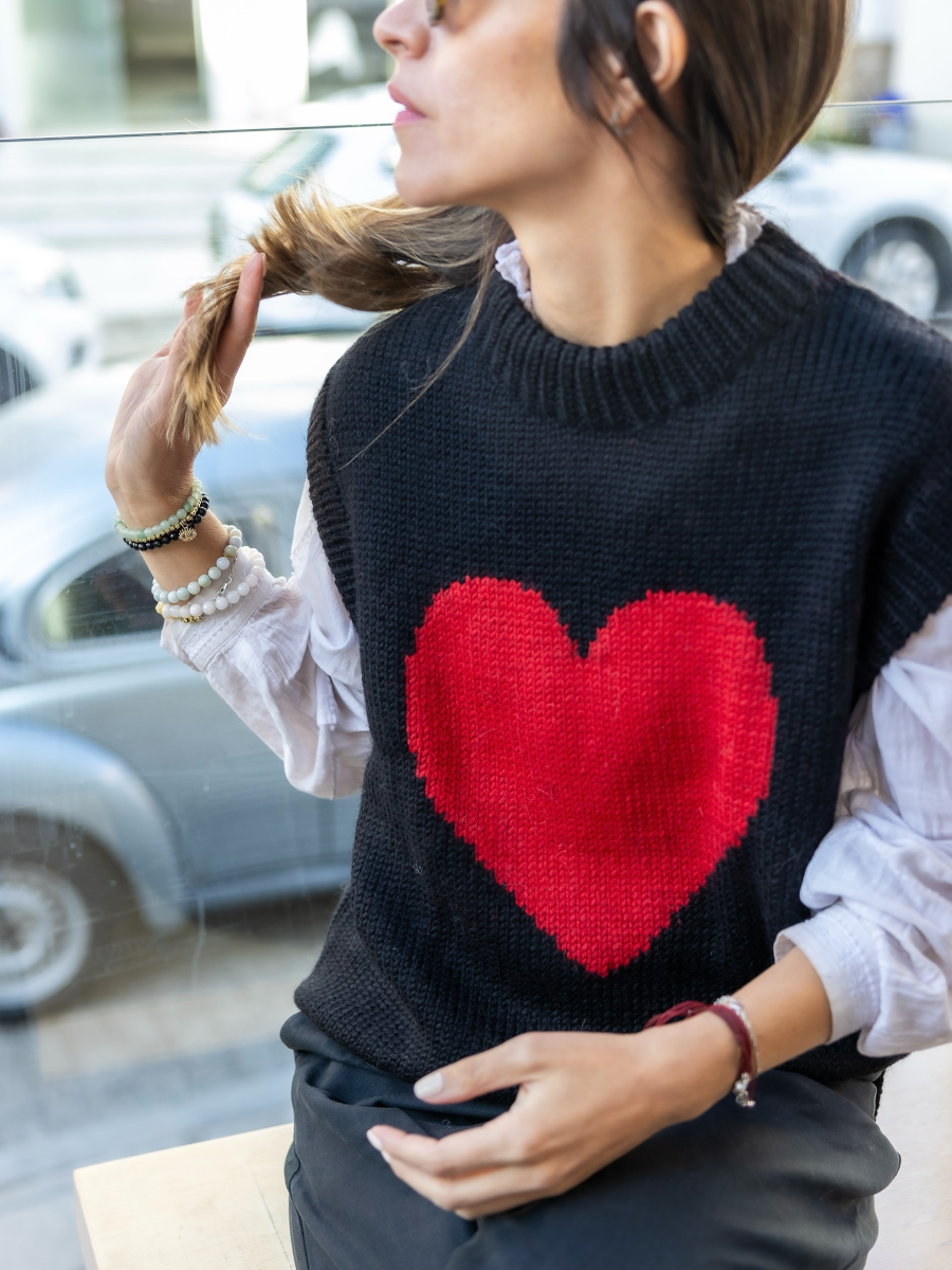 Woman wearing a black knitted vest with a red heart over a white blouse with a city street background