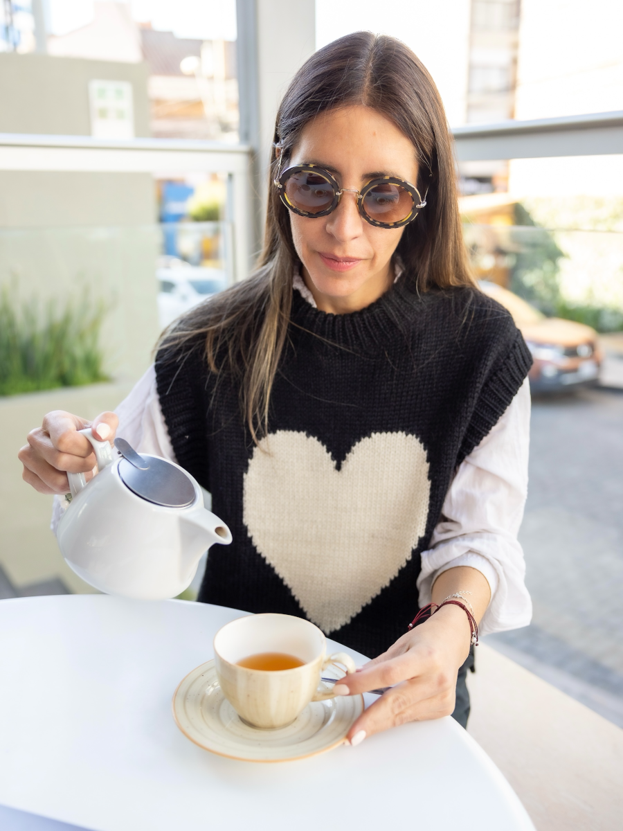 Woman wearing a black knitted vest with a white heart over a white blouse in a coffee shop 
