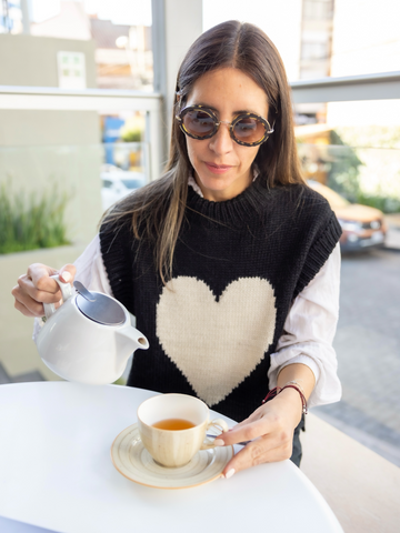 Woman wearing a black knitted vest with a white heart over a white blouse in a coffee shop 