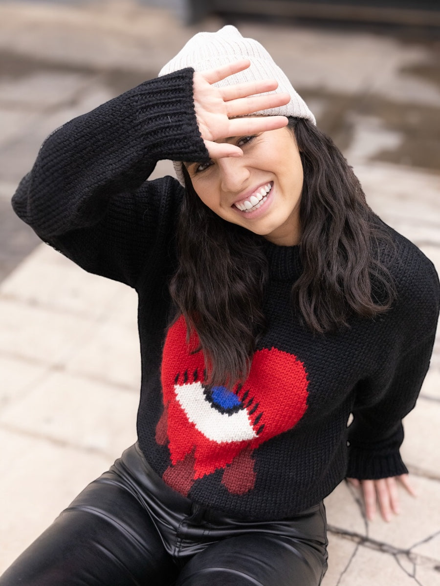 black alpaca sweater featuring a bold red heart motif with a blue eye and tear details on the front, shown here on a model.