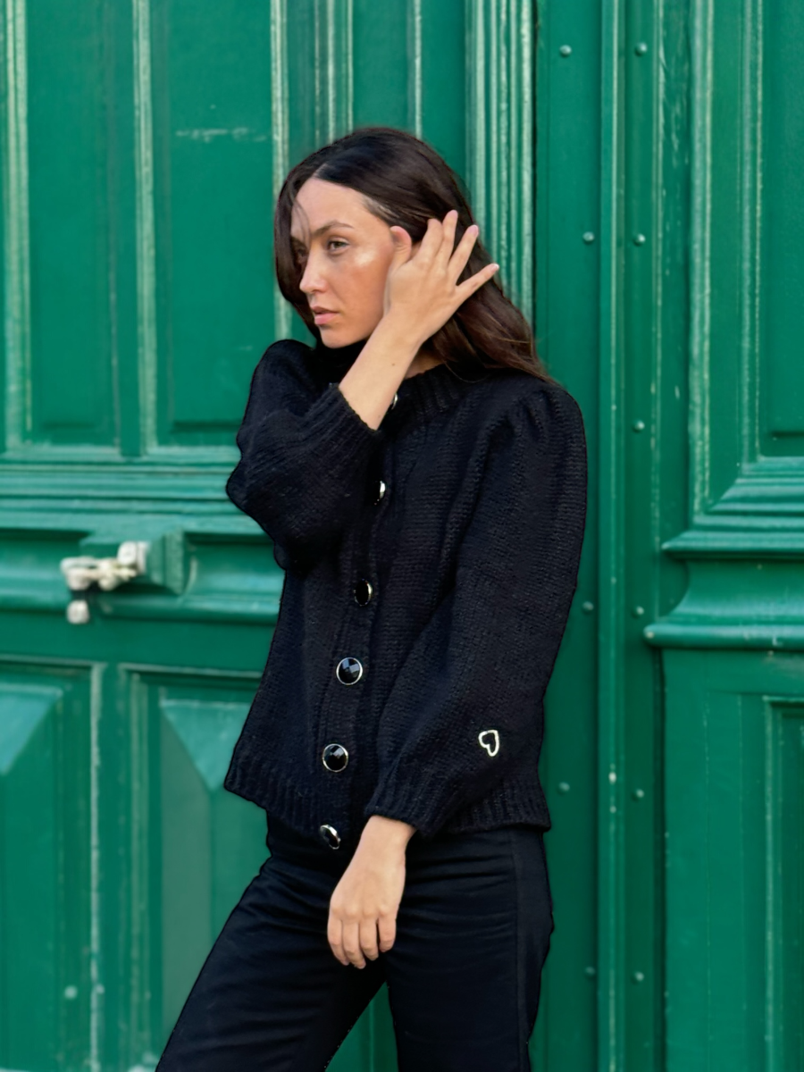 black chunky alpaca knitted cardigan with large round buttons, worn by a model against a green door
