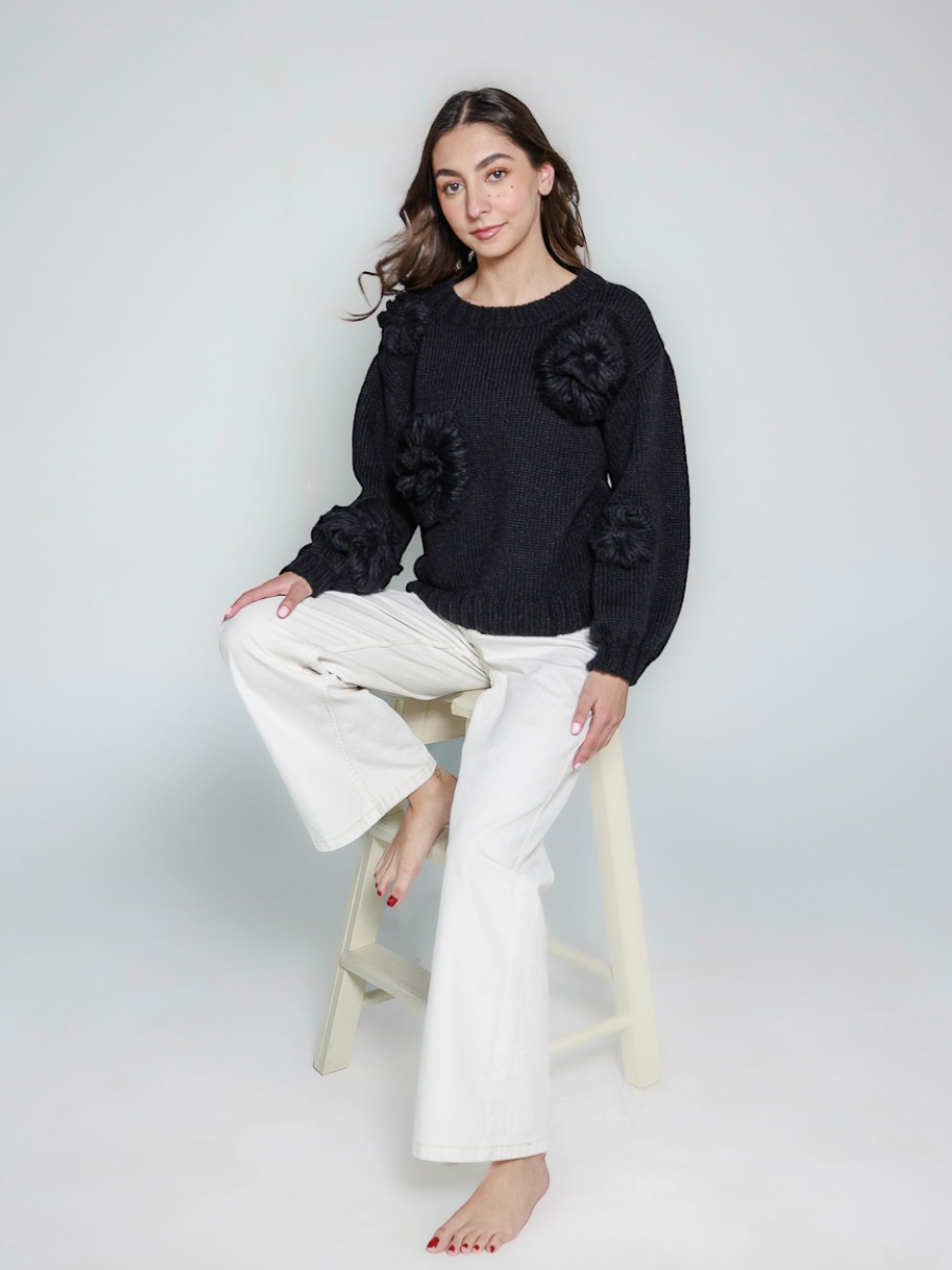 black llama hand-knitted sweater with floral embellishments, worn by a model against a white background