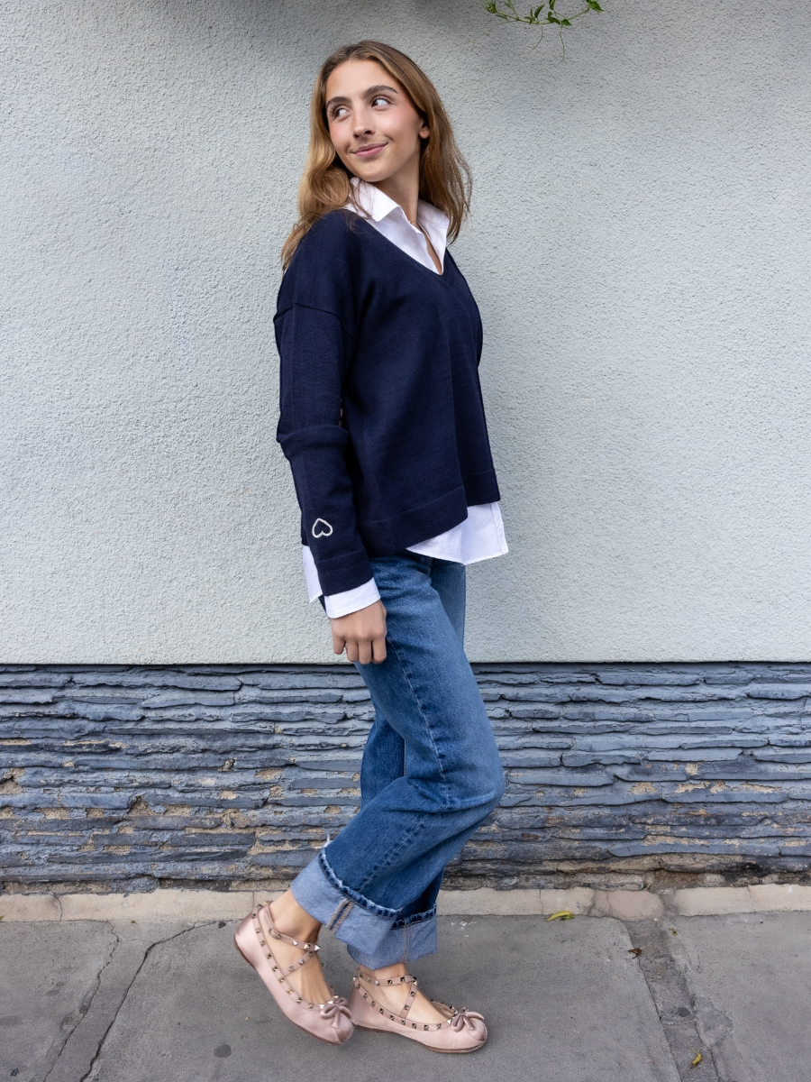 Navy blue alpaca sweater featuring a small embroidered heart on the sleeve, shown here on a model against a plain background. This reversible design can be worn as a V-neck on one side or flipped to a classic round neck on the other, offering two looks in one piece.