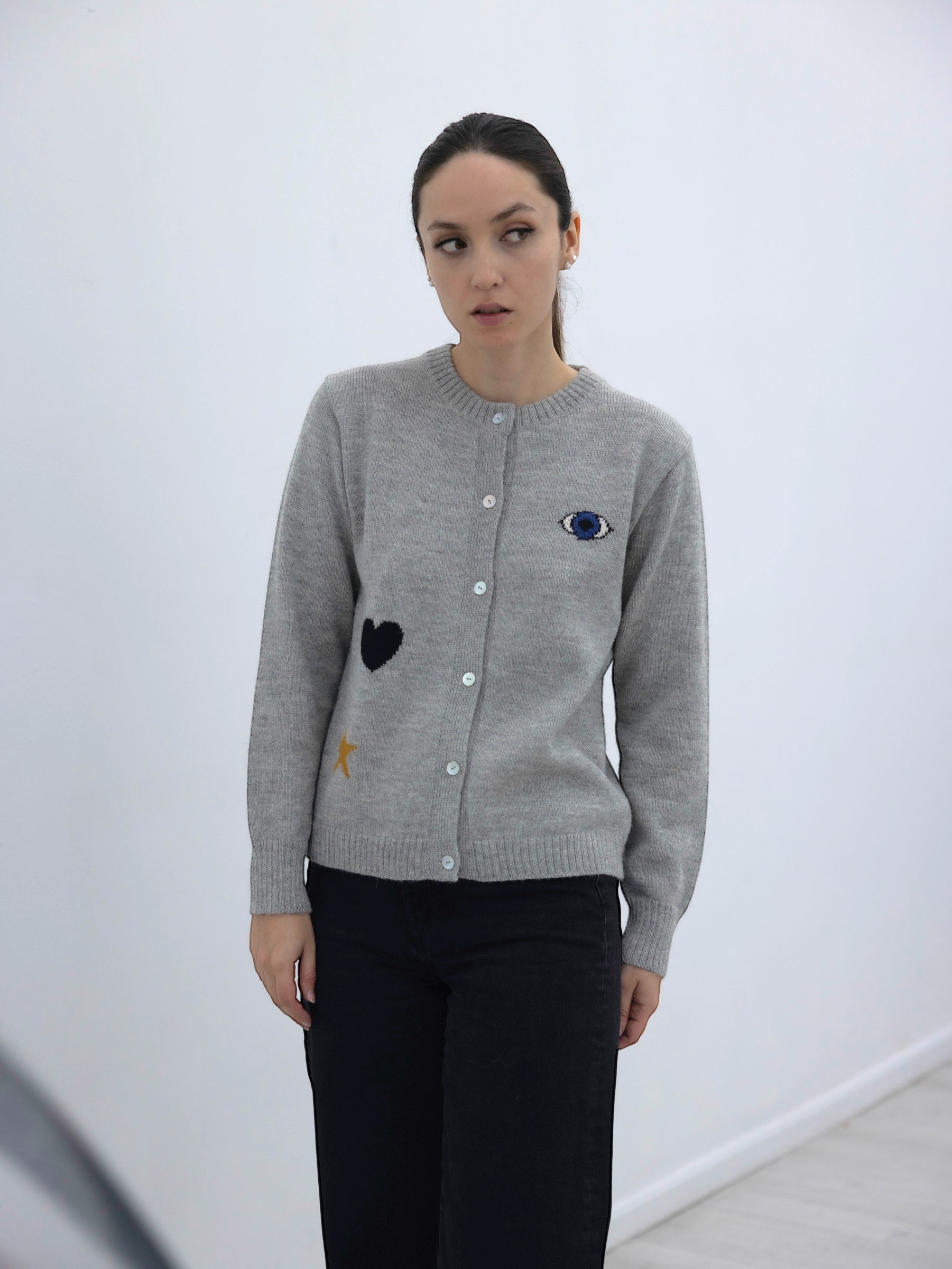 Woman wearing a gray cardigan with an eye a heart and a star design on a white background
