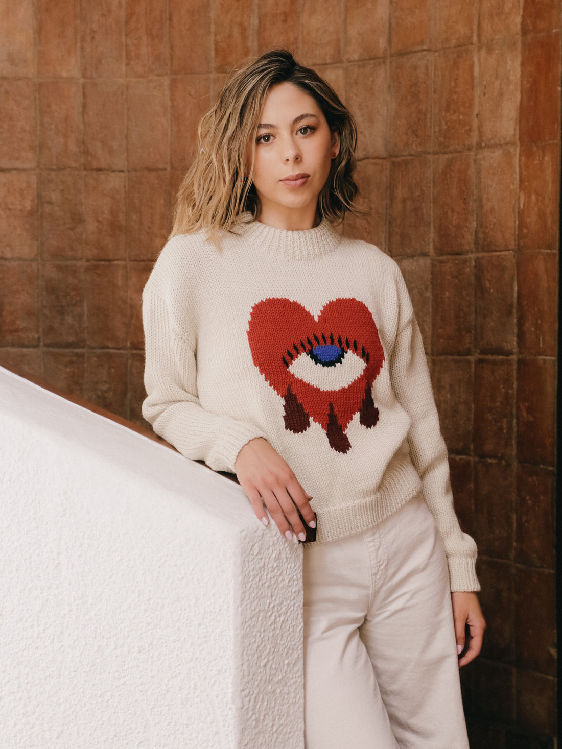 Woman wearing a sweater with a red heart design against a wooden wall.