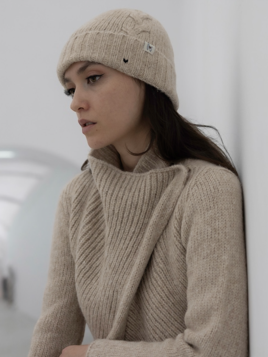 chunky beige llama knitted cardigan with unique crossed design, worn by a model styled with beige yapa beanie