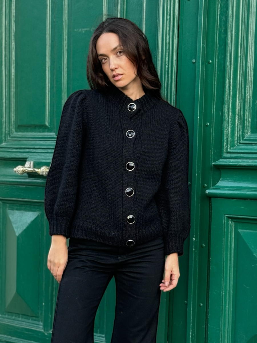 black chunky alpaca knitted cardigan with large round buttons, worn by a model against a green door
