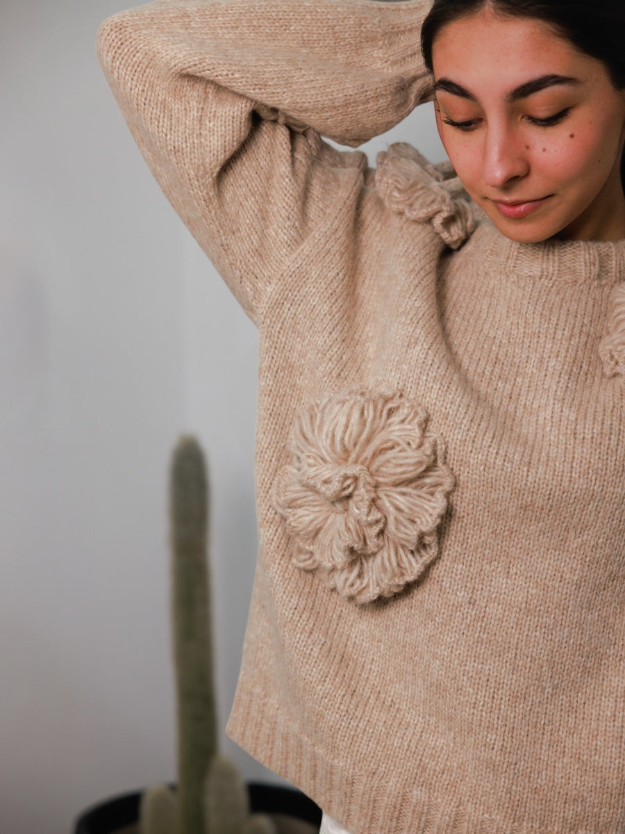 Woman wearing a beige sweater with floral embellishments